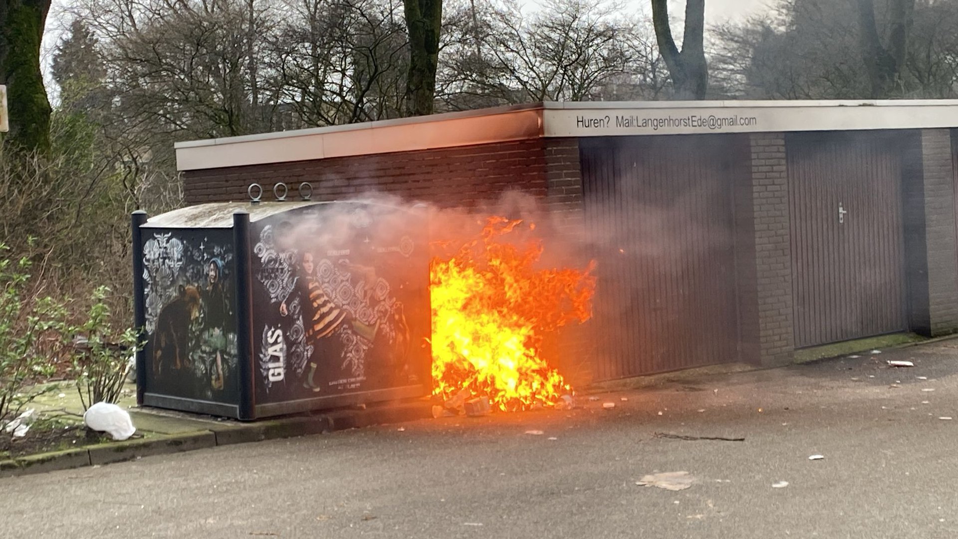 Berg met afval in brand gestoken naast garagebox