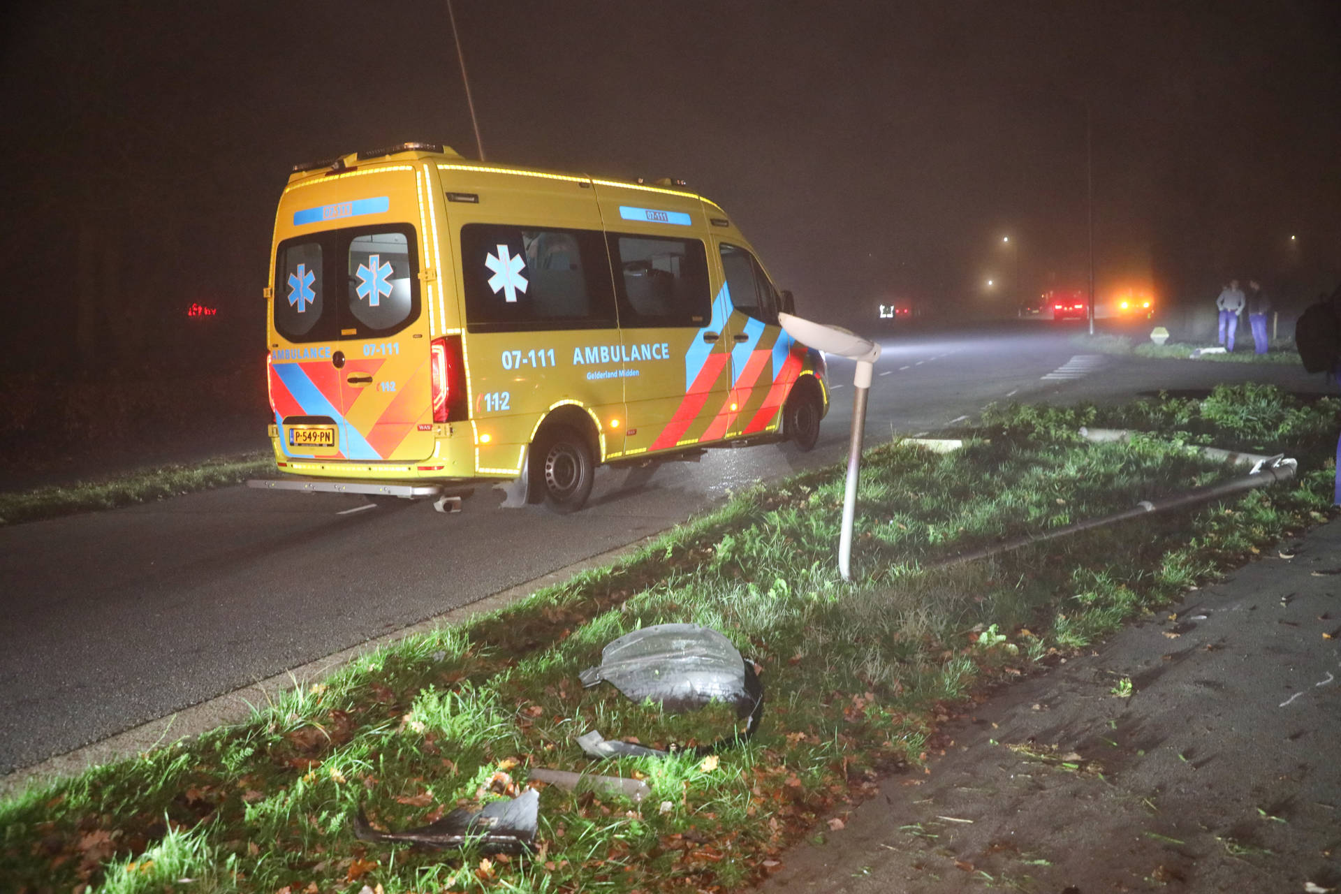 Auto rijdt lantaarnpaal omver; brommerrijder ziet obstakel te laat en raakt gewond