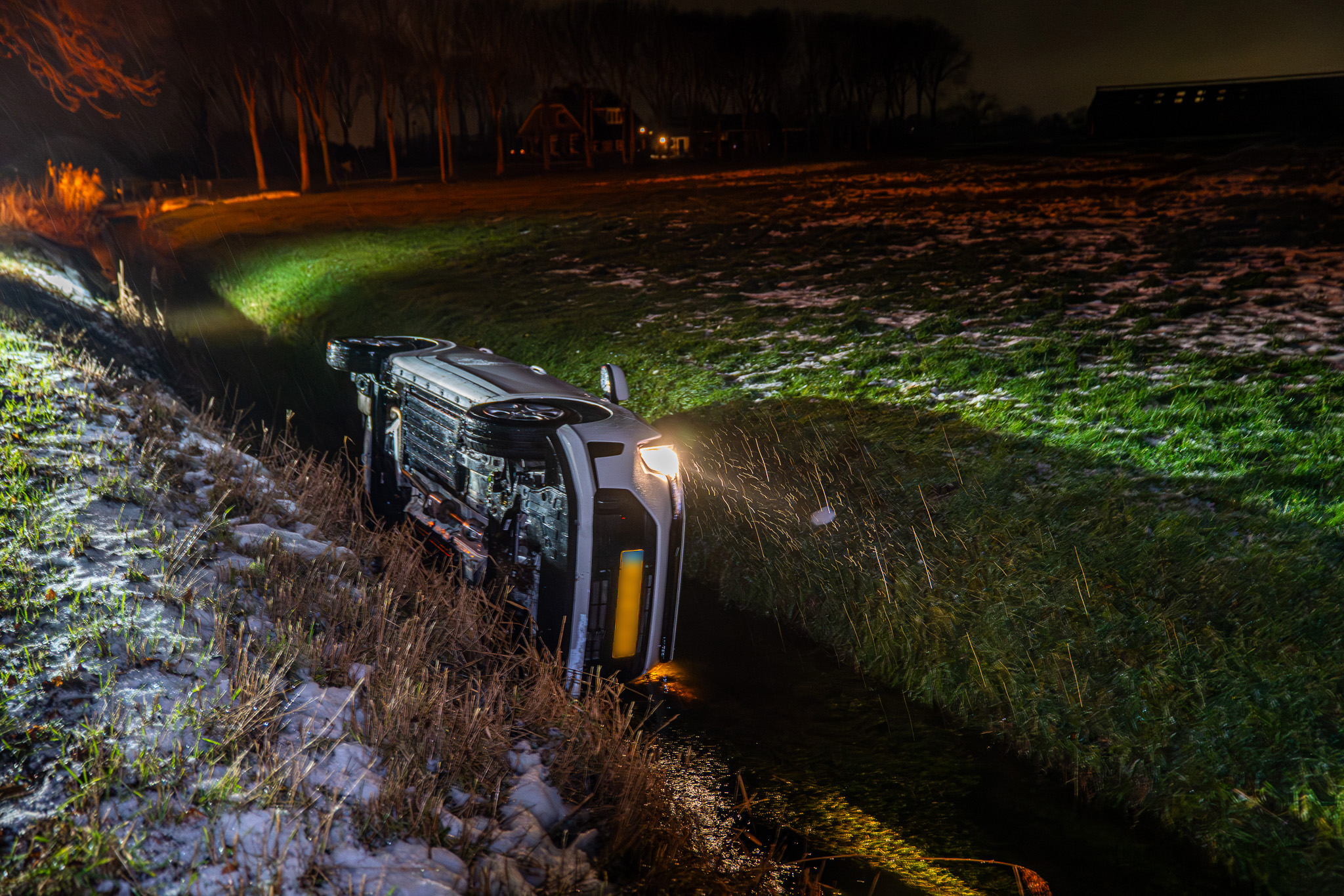 Auto glijdt door ijzel van weg en belandt op zijkant in sloot